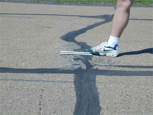 Close-up photo of a transverse joint with a slight but visible swell in the pavement surface at the joint.            A ruler has been placed across the joint in the longitudinal direction to show that there is an upward bulge in the pavement at the joint.