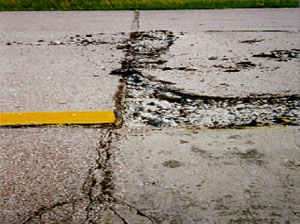 Overview photo of a transverse PCC joint with a medium-severity blowup.  Both slabs show some distress at the joint, but the right slab has considerable spalling due to the blowup.