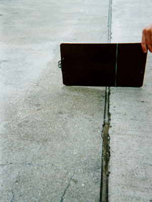 Close-up photo showing a transverse joint with a slight difference in elevation across the joint.            A clipboard is placed across the joint in the photo to illustrate that there is a height differential between the two slabs.