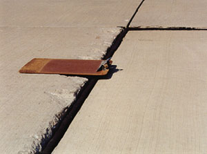 Close-up photo showing a transverse joint with a 1/2 in (13 mm) difference in elevation across the joint.            A clipboard is placed across the joint in the photo to illustrate that there is a height differential between the two slabs.