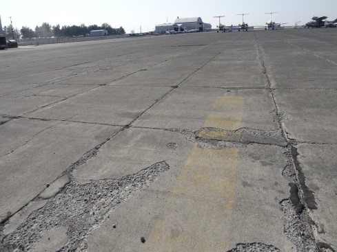 This picture shows an overview photo of an older PCC pavement with large areas of surface scaling.  Also almost every joint shows signs of joint spalling and deterioration.  The PCI of the pavement in the image is 5.