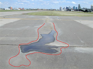 Photo showing a low-severity depression with standing water in it.            A red line has been drawn on the photo to outline the area with the depression.