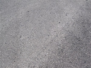 Close-up photo of a small area of asphalt pavement surface with a few missing pieces of aggregate.