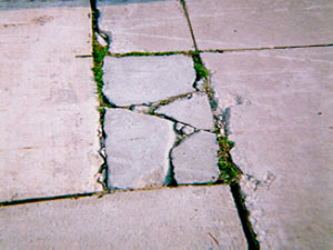 Close-up of a rectangular PCC patch that is divided into more than five pieces.            The cracks that divide the patch into the different pieces are very wide high-severity cracks.